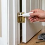 Hand applying lubricant to a squeaky door hinge on a white interior door